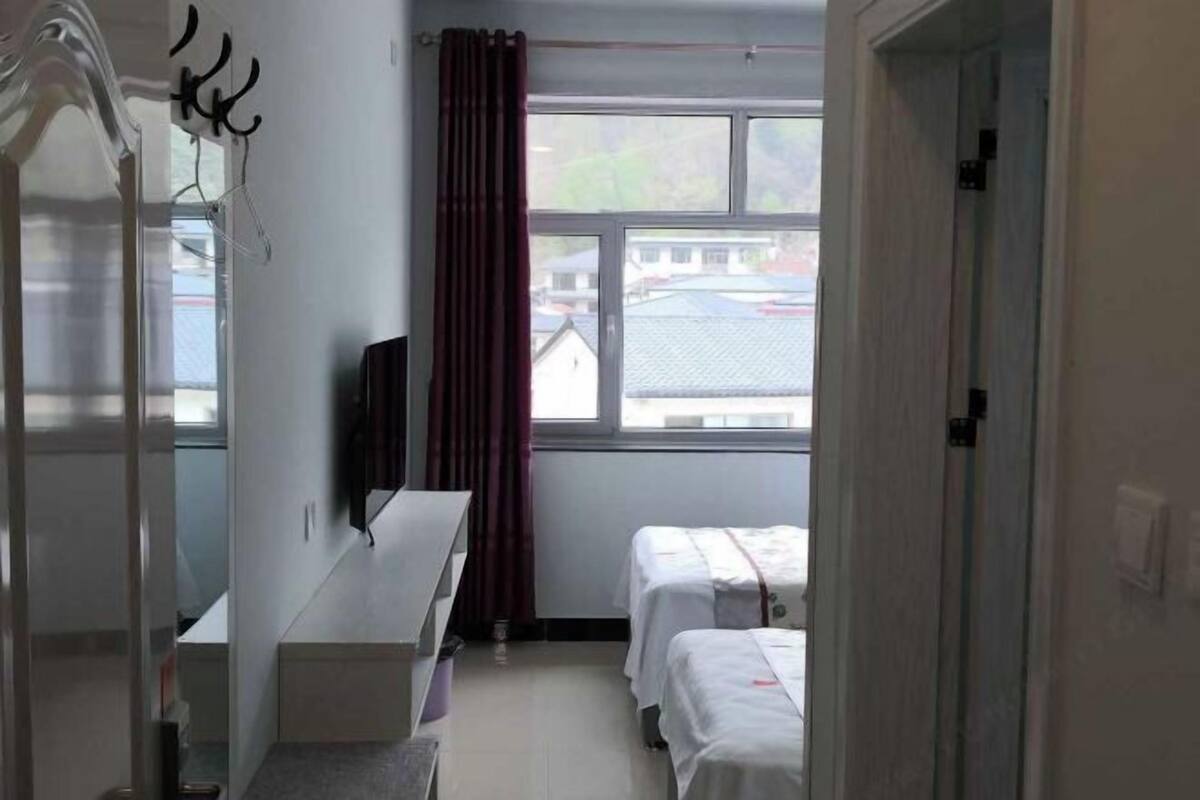 Habitación de hotel con escritorio, dos camas, televisor y ventana con cortinas.