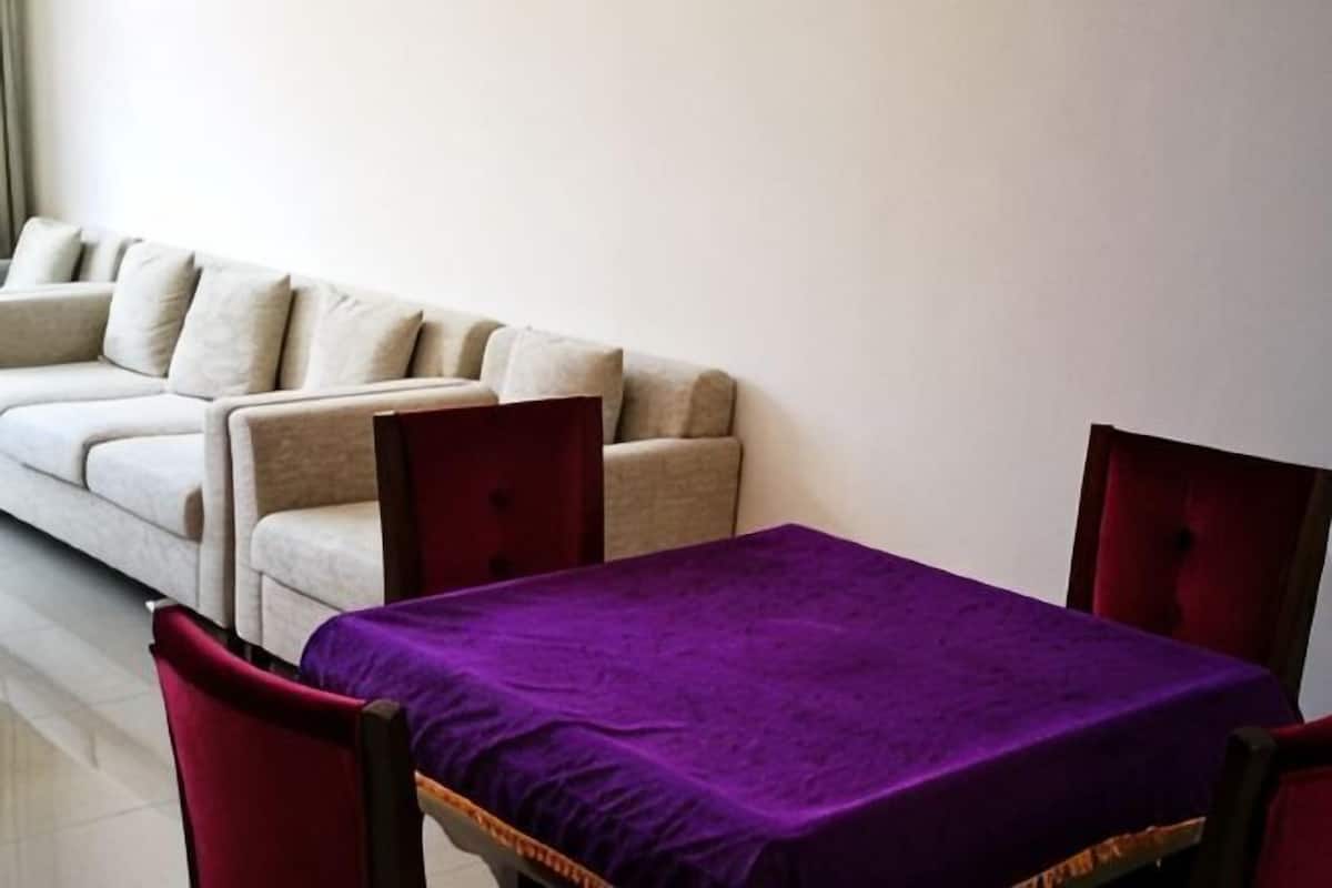Una habitación con un sofá, una mesa con mantel morado y dos sillas.
