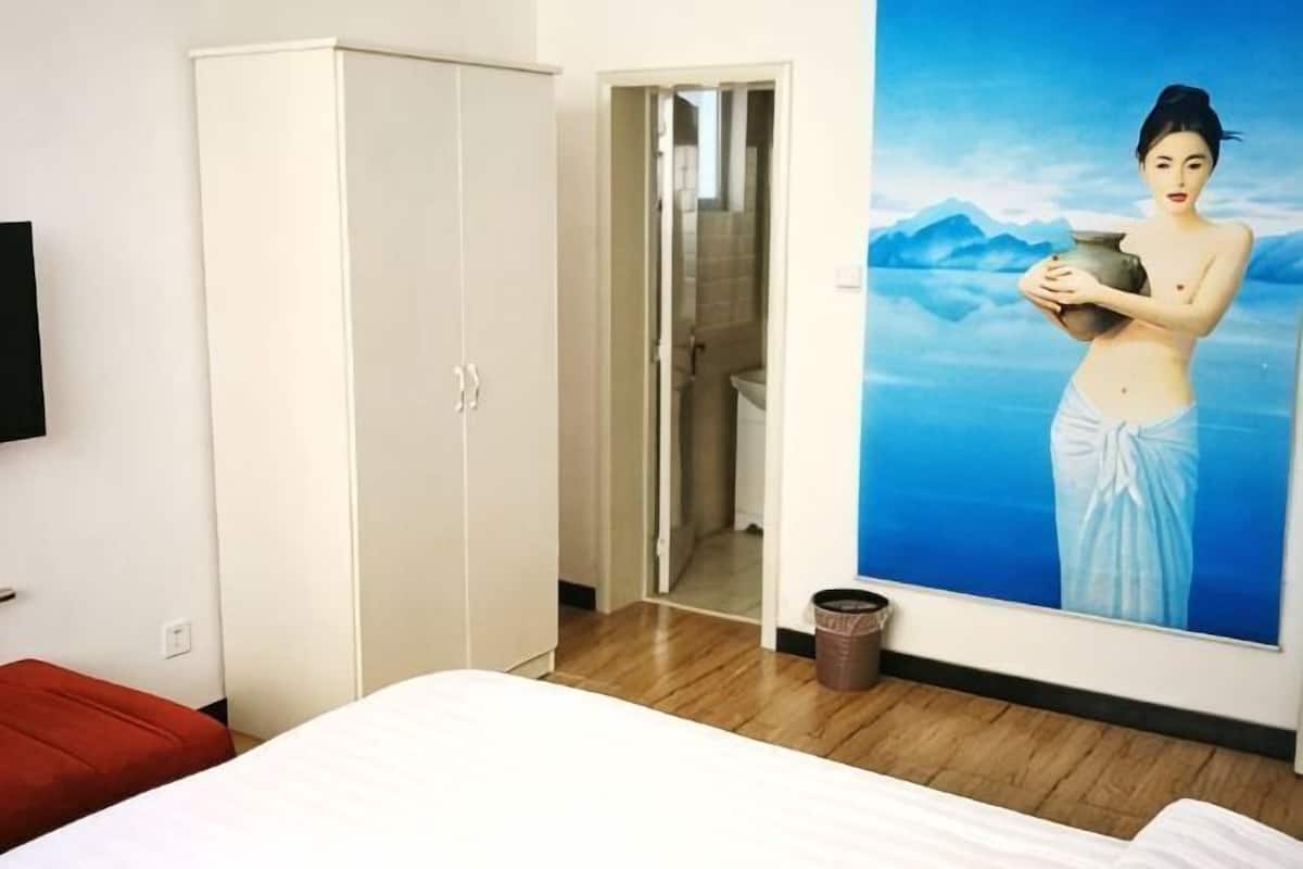 Un dormitorio con cama, armario, un cuadro y una puerta que da al baño.