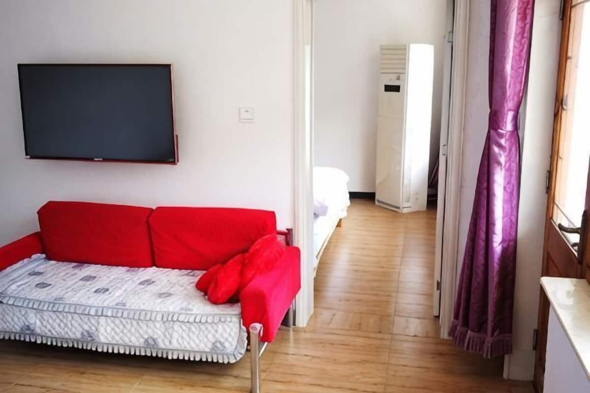 Una habitación con un sofá rojo, un televisor de pantalla plana, una puerta blanca y una cortina morada.