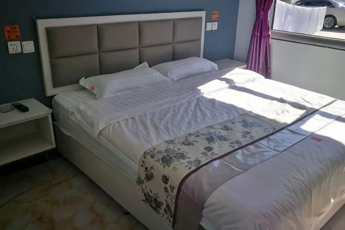 Una cama con cabecera, una mesita de noche y una ventana con cortina.