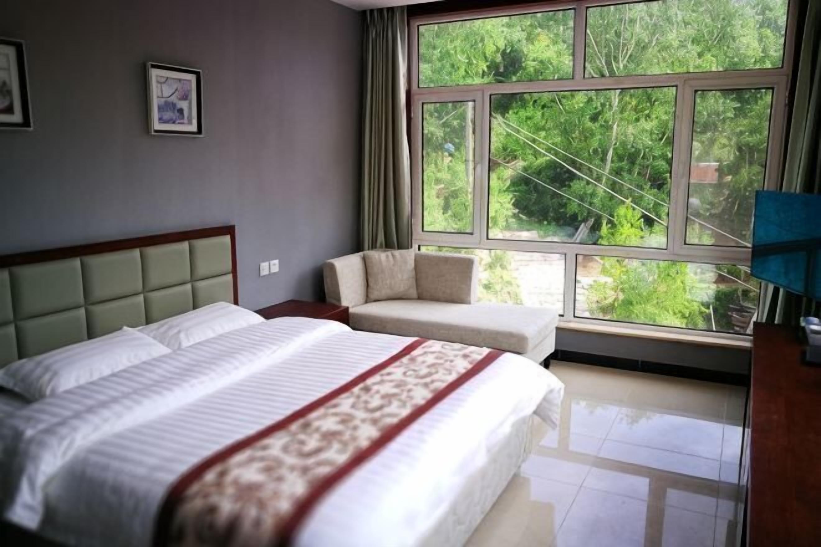Un dormitorio con cama, sofá, ventana y vista a follaje.