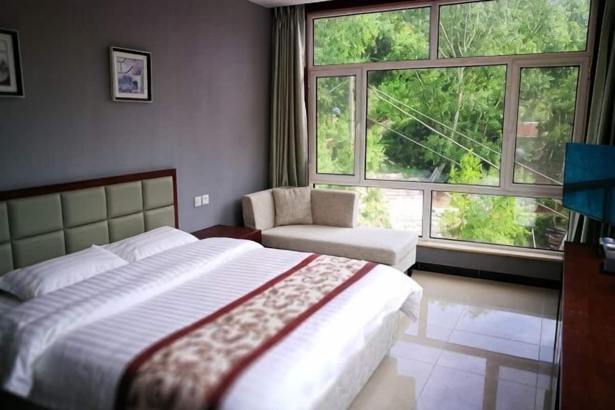 Un dormitorio con cama, sofá, ventana y vista a follaje.