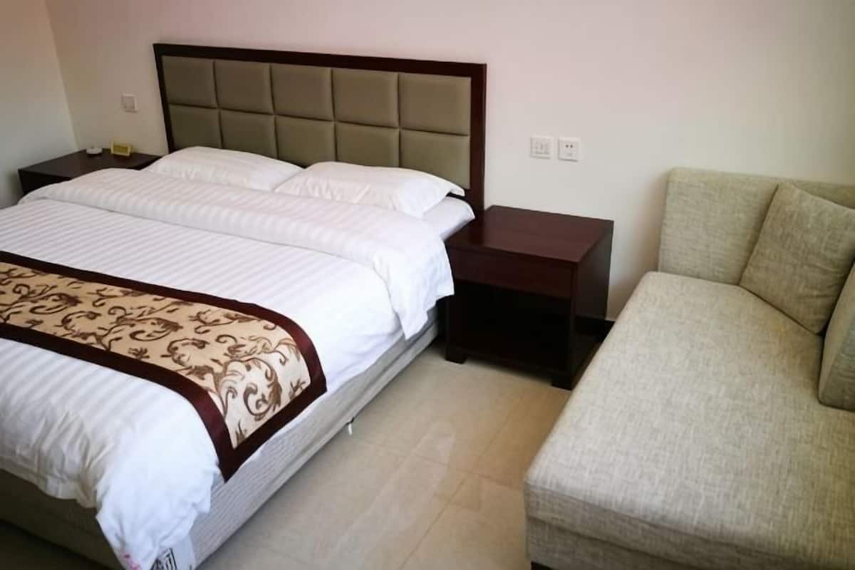 Un dormitorio con cama, mesitas de noche, un sofá y una manta estampada.