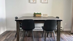 A dining area with a wooden table, two black chairs, and two framed botanical prints on the wall.