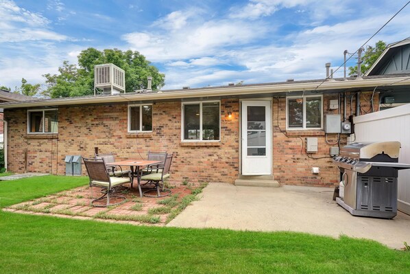 Une maison en briques avec un patio, un barbecue et un espace extérieur aménagé avec des sièges, protégé par un auvent.