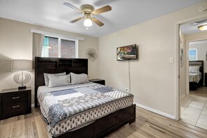 Une chambre à coucher comprenant un lit, une table de chevet, un ventilateur de plafond, une fenêtre et une porte.