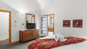 A bedroom with a bed, dresser, TV, and artwork.