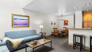 A compact living space with a sofa, coffee table, dining table, chairs, a kitchen area, and a hanging light fixture.