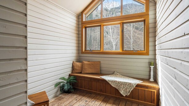 A cozy corner with a wooden bench, a small table, and a window with a view of trees.