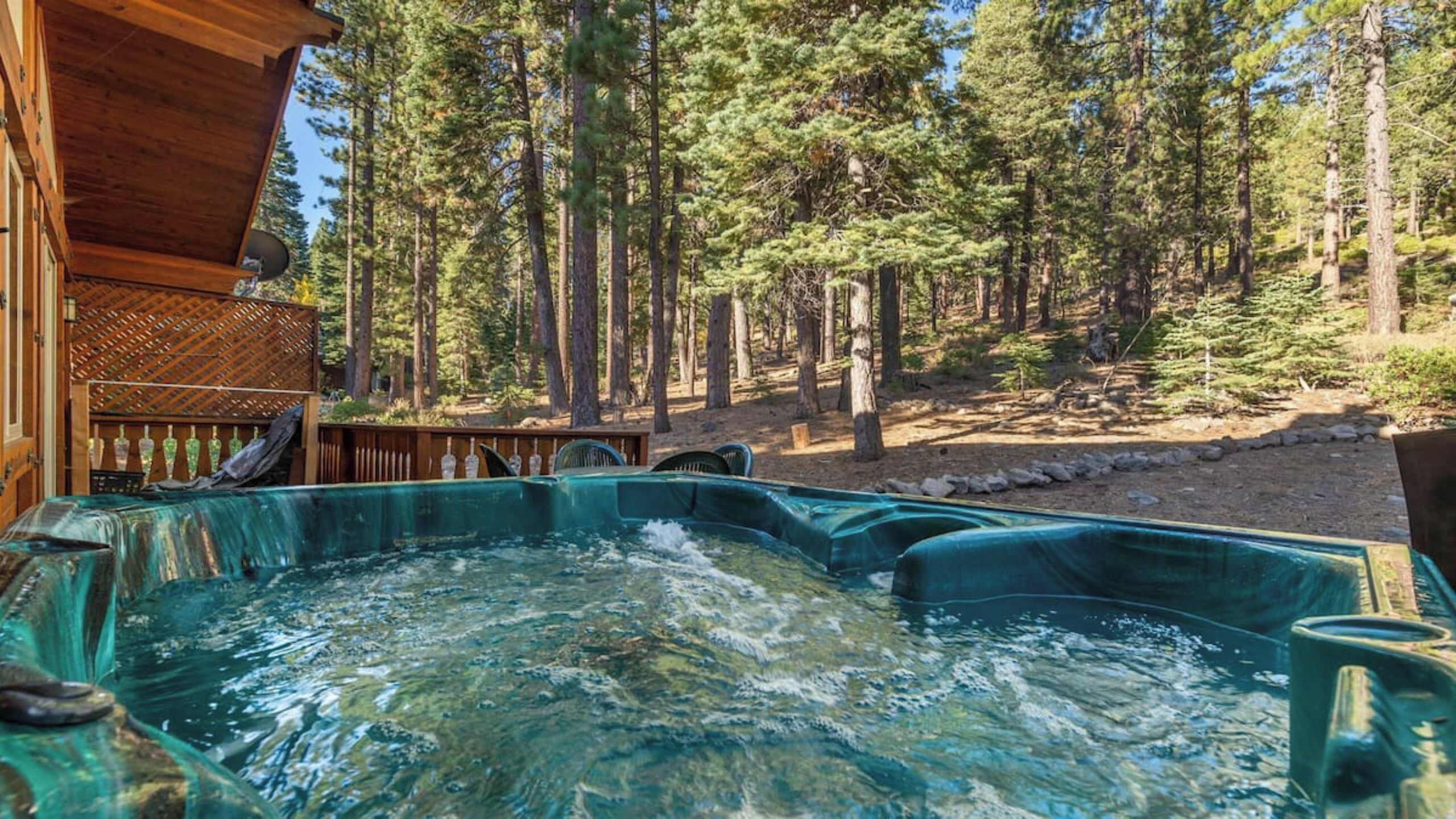 A hot tub surrounded by a wooden deck, with a forested area in the background.