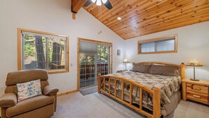 A bedroom with a wooden ceiling, a bed with a patterned blanket, a chair with a floral pillow, and a nightstand with a lamp. - Wolf's Lair by Avantstay Swiss Chalet w/ Private Hot Tub & Access to Northstar Resort Community (Truckee)