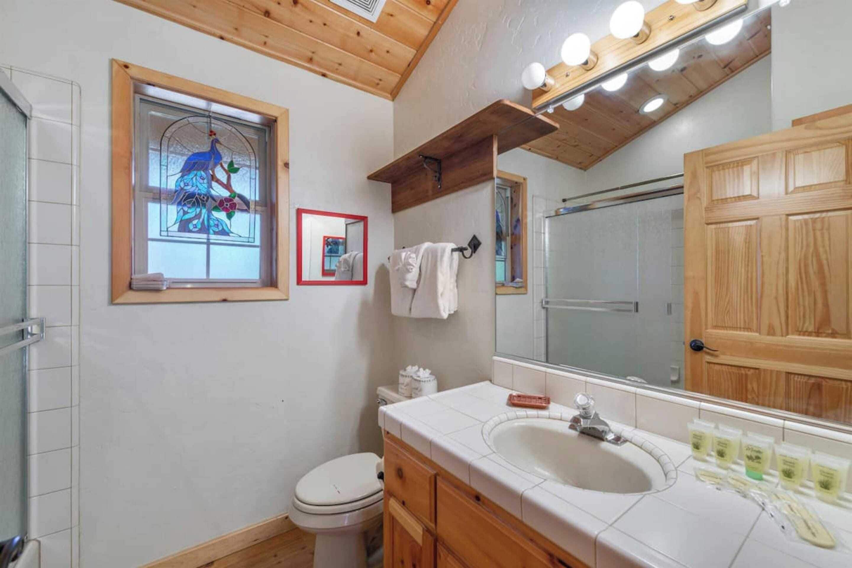 A bathroom with a wooden ceiling, a large mirror, a sink, and a toilet.
