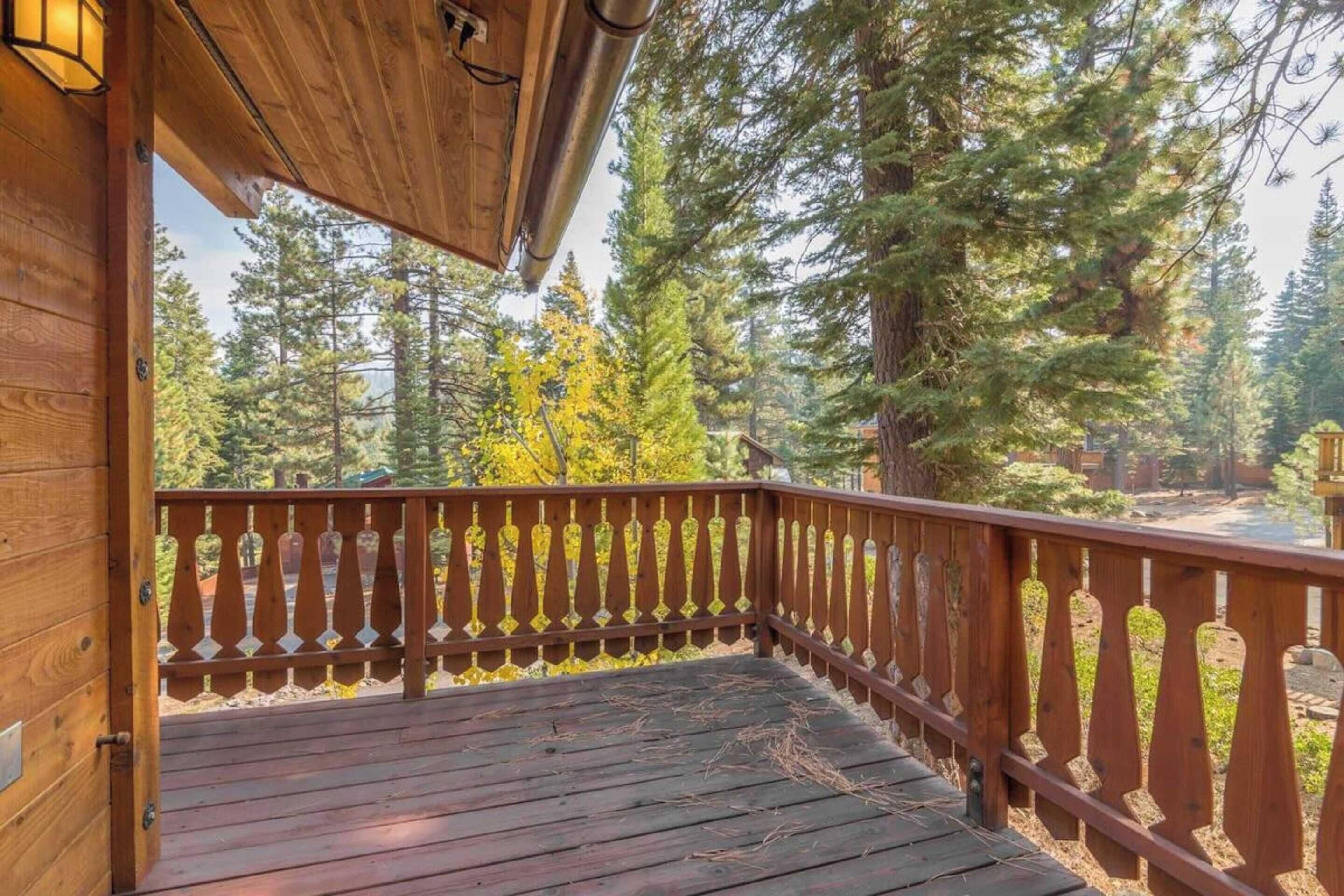 Une terrasse en bois avec une rambarde, entourée d’arbres et offrant une vue sur une forêt.