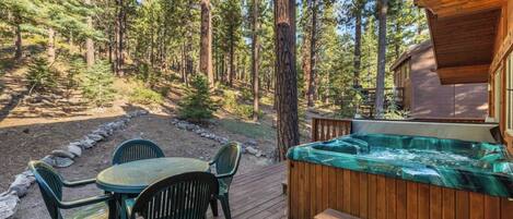 A wooden deck with a hot tub, outdoor seating, and a view of a forested area.