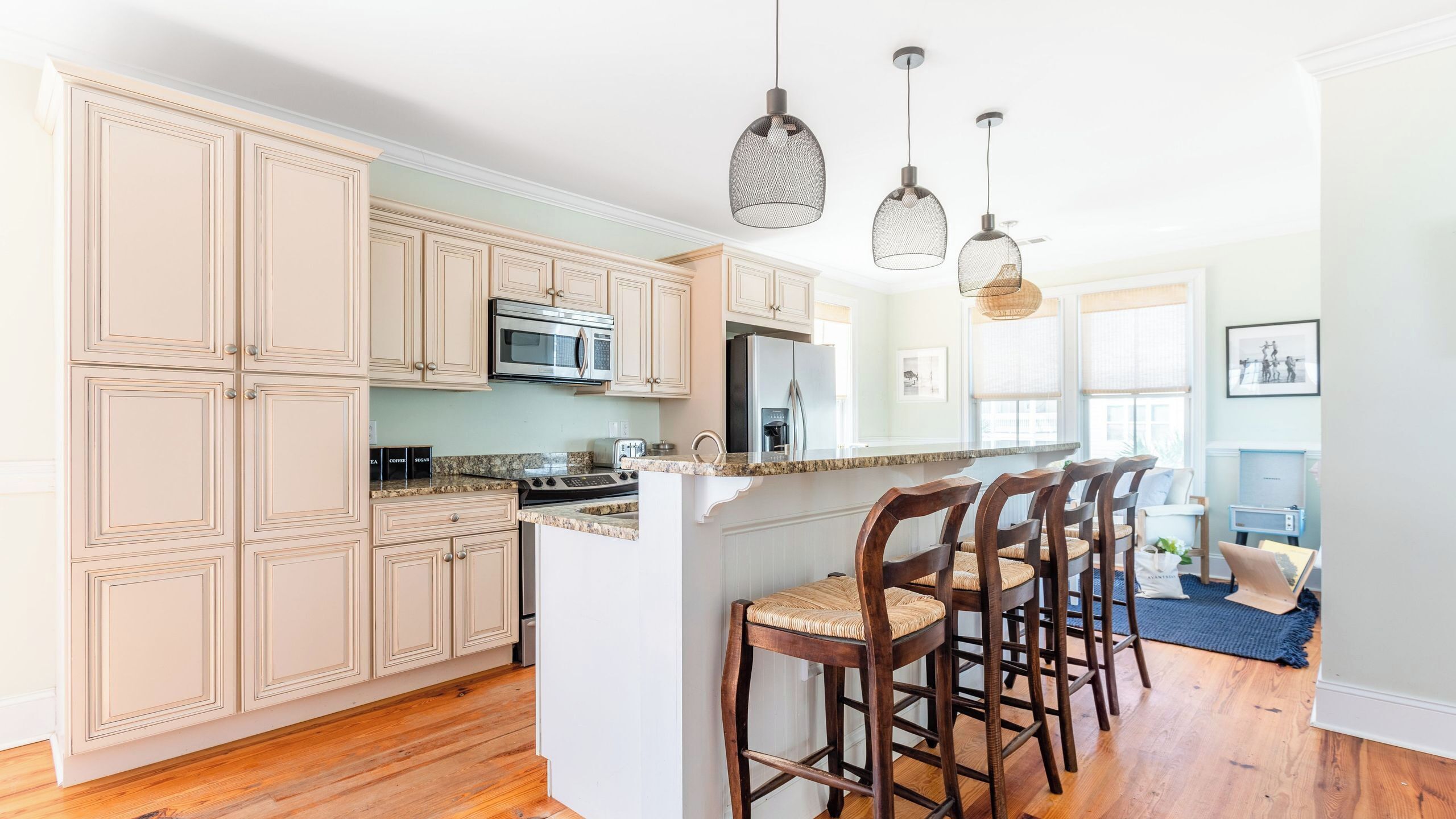 A kitchen with wooden cabinets, a central island with bar stools, a microwave, and a refrigerator.
