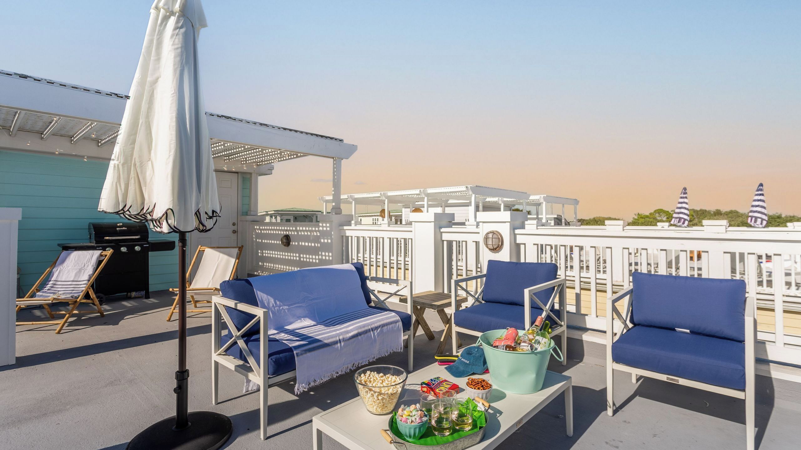 Une terrasse sur le toit avec des chaises longues bleues, un barbecue et un espace aménagé au bord de la piscine.