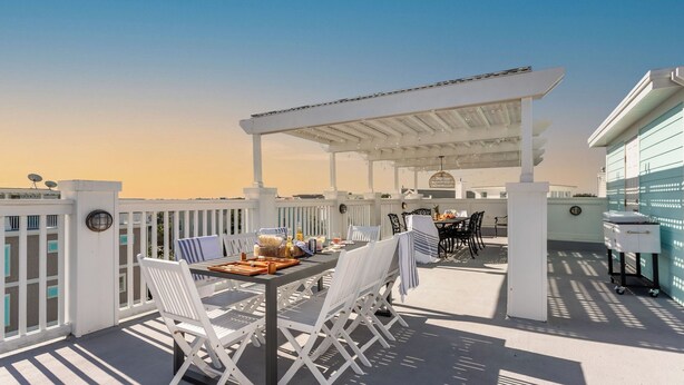 An outdoor patio with a table set for dining, white chairs, and a pergola. - Sea Shell by Avantstay Breezy Beachside Getaway w/ Rooftop Deck & 6 BRs (Isle of Palms)