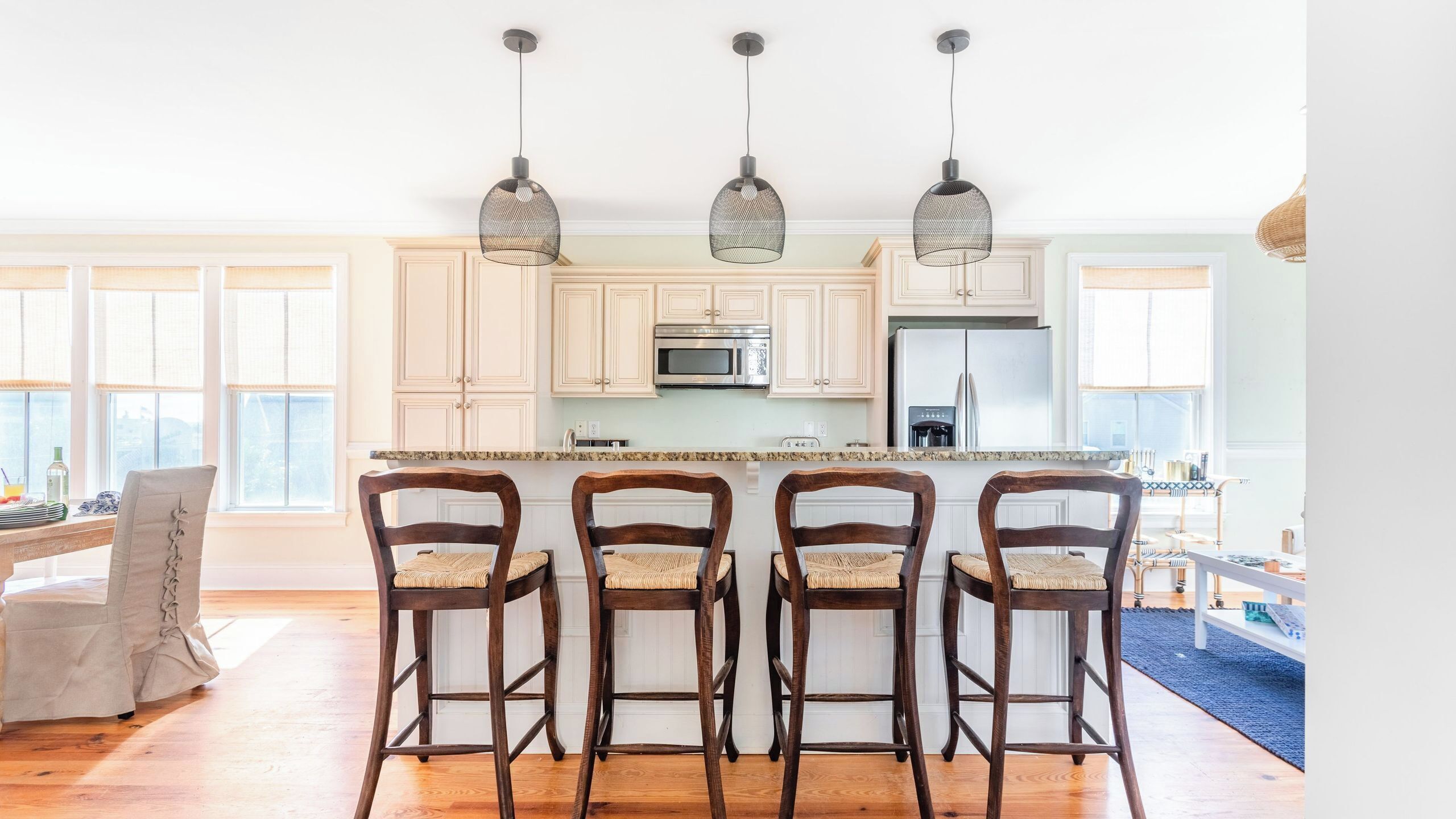 A kitchen with four wooden bar stools, a central island, and pendant lights.