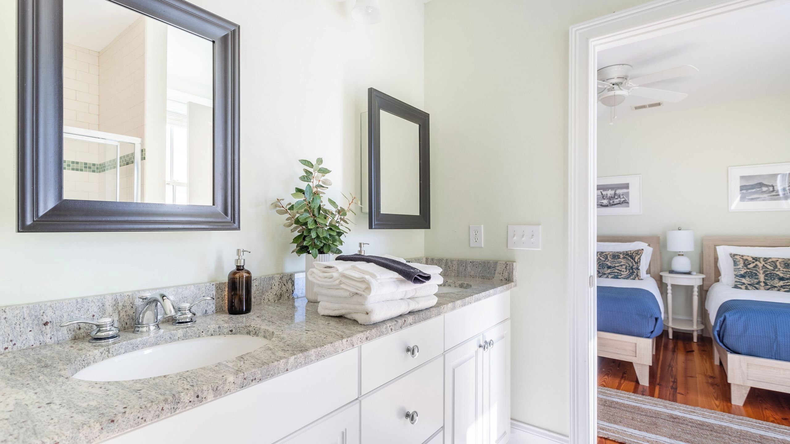 Une salle de bain avec un lavabo, deux miroirs, une plante et une pile de serviettes.