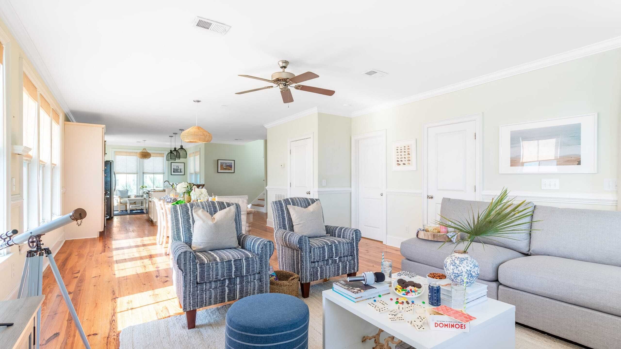 A spacious living room with a large window, a ceiling fan, and a dining area with a table and chairs.