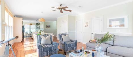A spacious living room with a large window, a ceiling fan, and a dining area with a table and chairs.