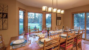 A dining area with a wooden table set for six, large windows, and a chandelier.