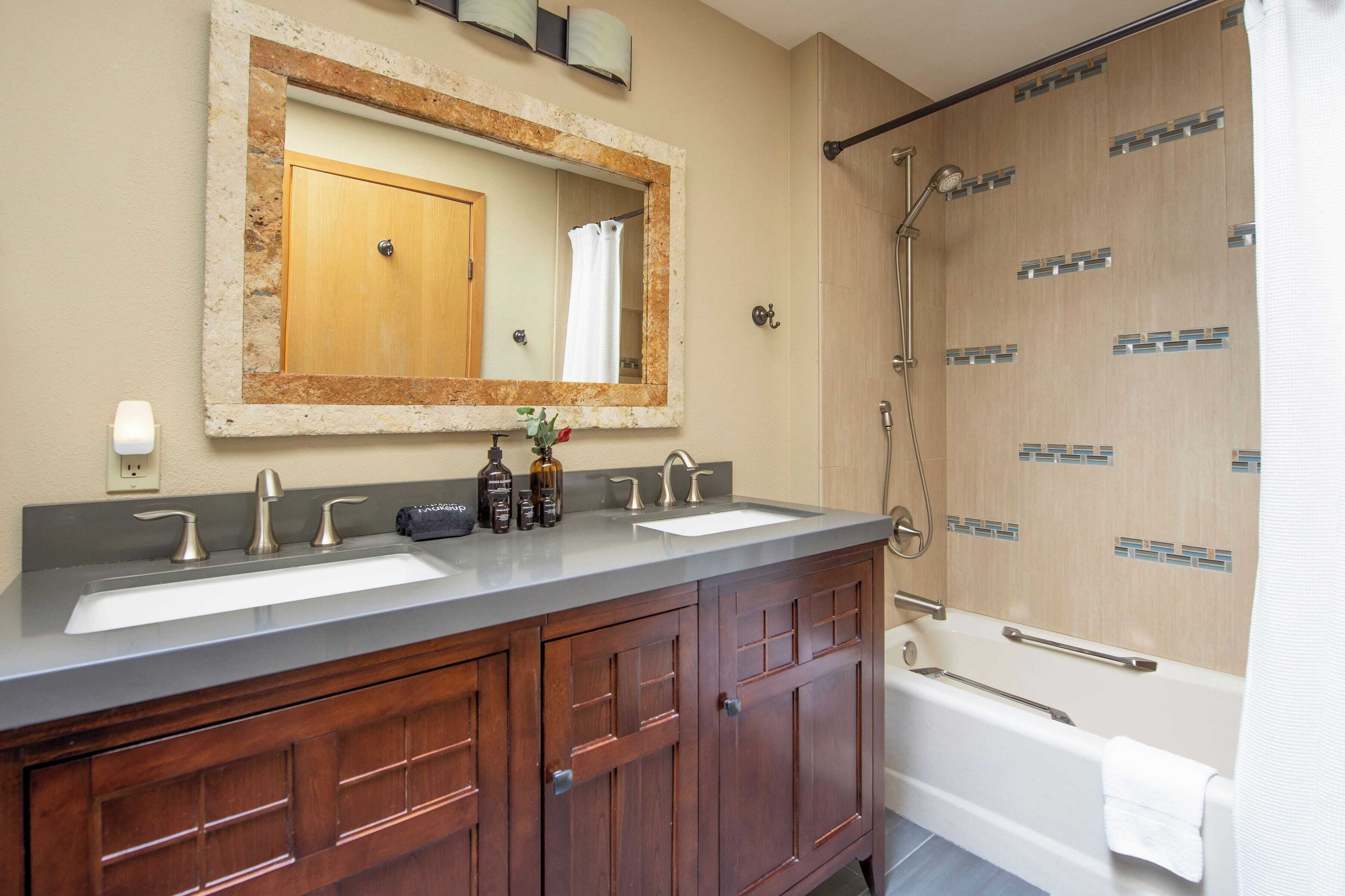 A bathroom with two sinks, a large mirror, wooden cabinets, and a walk-in shower.
