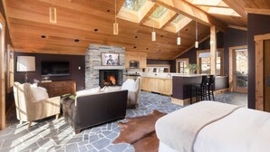 A spacious living area with a fireplace, stone flooring, wooden ceiling, and a stone wall. - Hunter by Avantstay Award-winning Riverfront Cabin 5 Minutes From Palisades (Truckee)