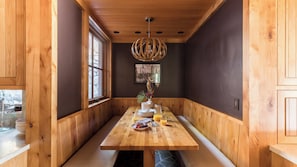 A wooden dining area with a bench, a table set with plates, glasses, and a pitcher, and a hanging light fixture.