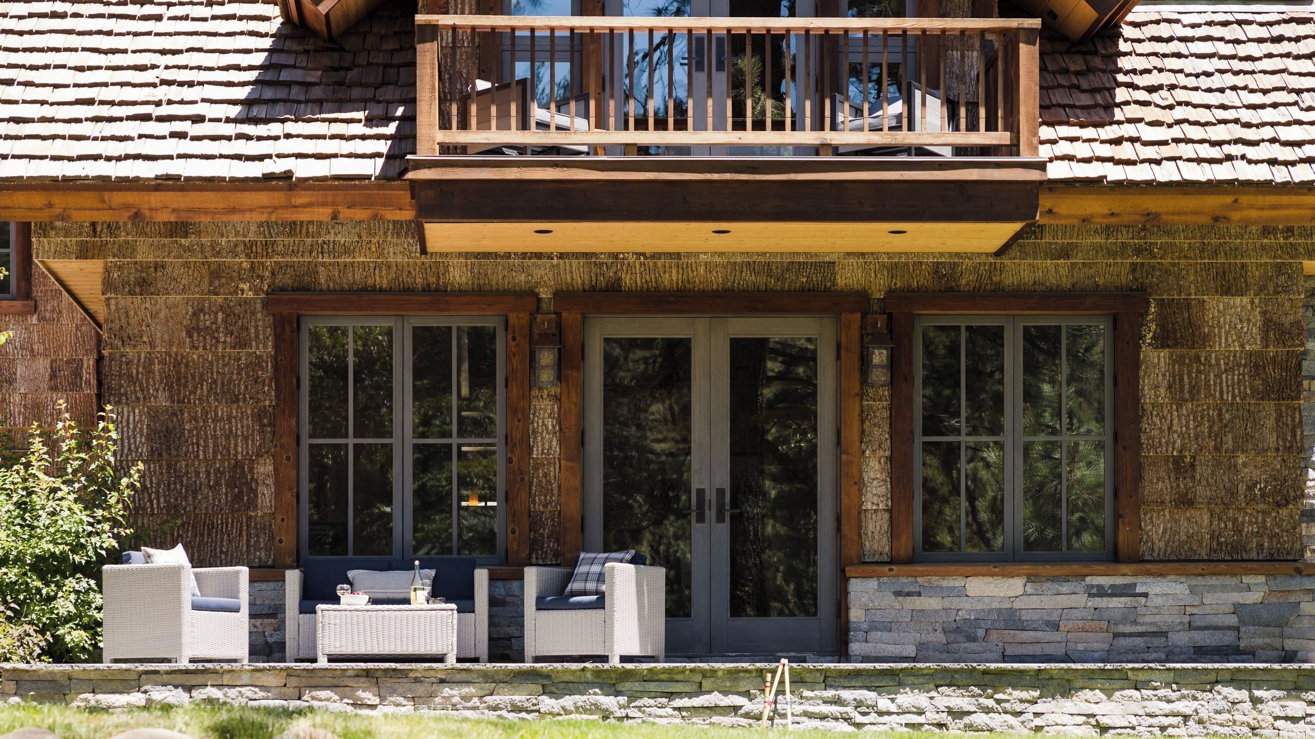 A two-story house with a balcony, large windows, and outdoor seating.