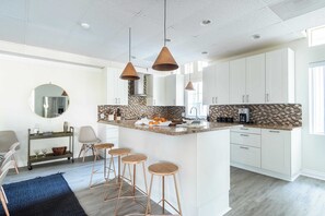 A modern kitchen with white cabinets, a central island with stools, pendant lighting, and a tiled backsplash. - Balboa II by Avantstay Modern Condo w/ Balcony & Views of Balboa Park! (San Diego)