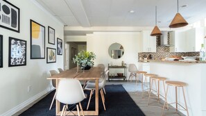 A modern kitchen with a central island, a dining area with a wooden table and chairs, and a living space with a sofa and a coffee table. - Balboa II by Avantstay Modern Condo w/ Balcony & Views of Balboa Park! (San Diego)