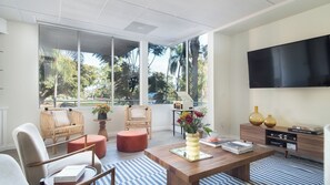A modern living room with large windows, wicker furniture, a coffee table, and a flat-screen TV. - Balboa II by Avantstay Modern Condo w/ Balcony & Views of Balboa Park! (San Diego)