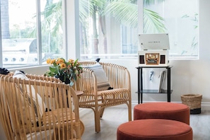A room with wicker chairs, a red ottoman, a radio, and a window with a view of palm trees. - Balboa II by Avantstay Modern Condo w/ Balcony & Views of Balboa Park! (San Diego)