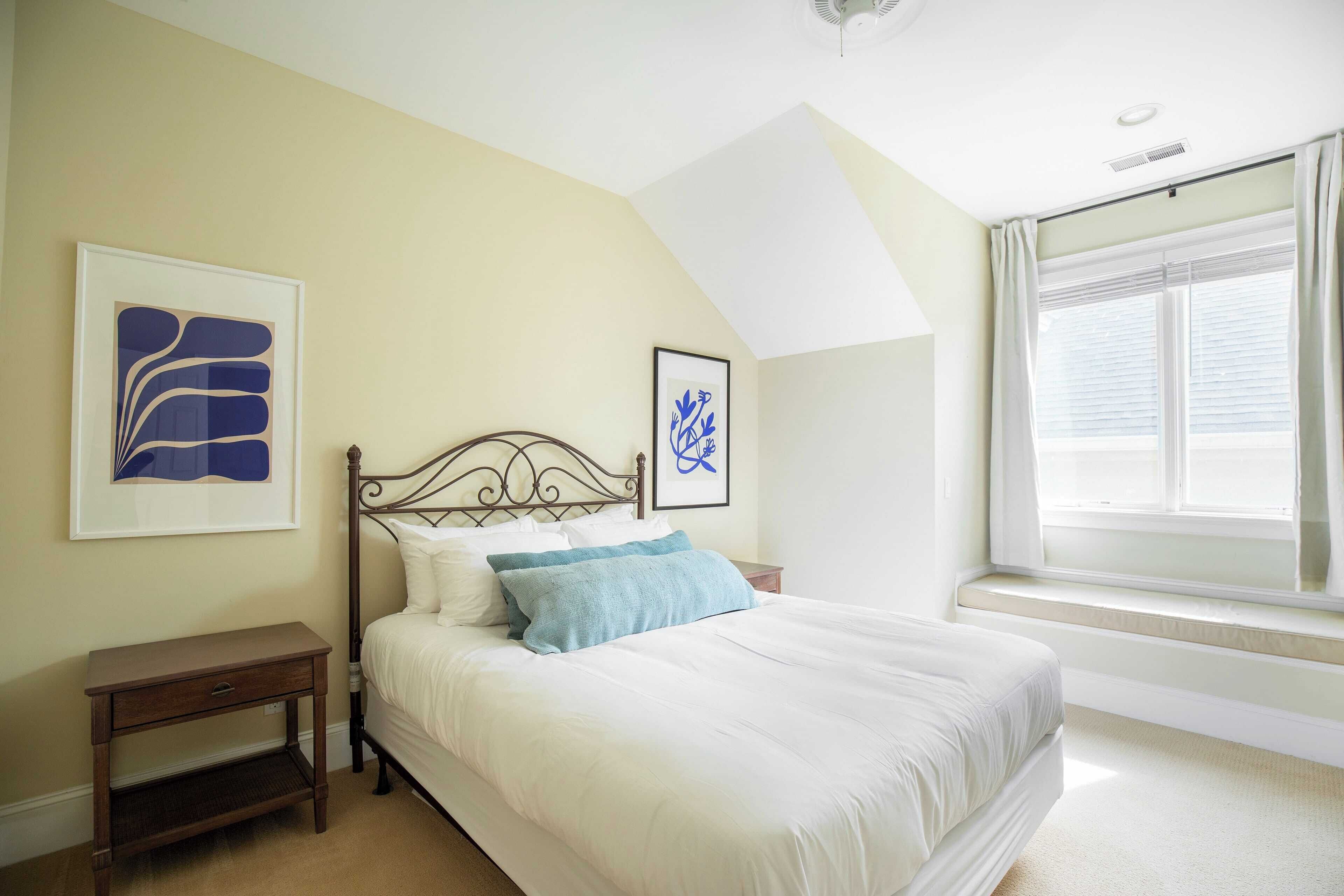 A bedroom with a bed, a nightstand, and two framed artworks on the wall.