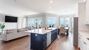A modern kitchen with a central island, a dining area with a view, and a living room with a sofa and a TV. - Oceanfront, Pool+hot Tub, Game Room, Views Steps to Beach Lido by Avantstay (Hilton Head Island)
