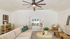 A spacious living room with a ceiling fan, a sofa, a coffee table, wicker furniture, and a view into the dining area.