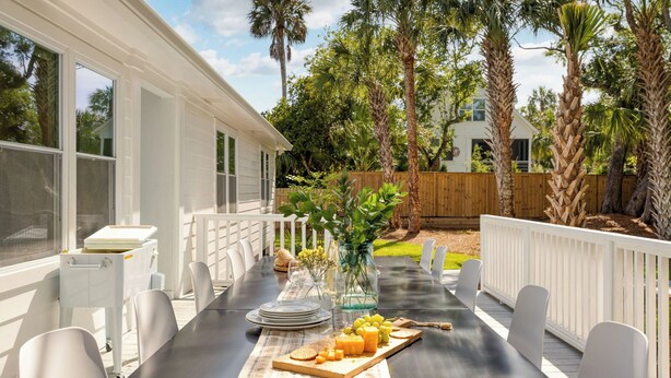 An outdoor dining area with a table set for four, surrounded by white chairs, a white fence, and a wooden deck.