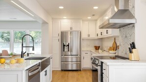 A modern kitchen with white cabinets, stainless steel appliances, and a large window.