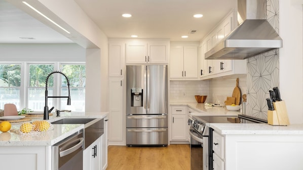 A modern kitchen with white cabinets, stainless steel appliances, and a large window.