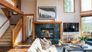 A spacious living room with a fireplace, a staircase, and a large window with a mountain view.