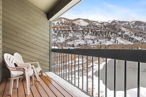 Um deck de madeira com duas cadeiras Adirondack com vista para uma paisagem montanhosa coberta de neve.