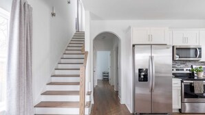Una cocina moderna con electrodomésticos de acero inoxidable, una escalera de madera y armarios blancos.