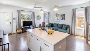 Una cocina moderna con una isla central, un comedor y un espacio de sala con un sofá y una televisión.