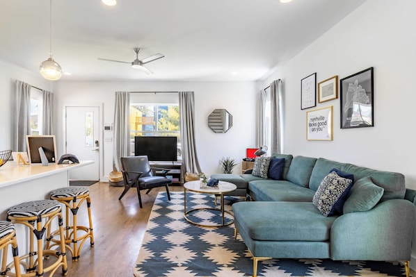A modern living room with a green sofa, black and white stools, a round coffee table, and a ceiling fan.