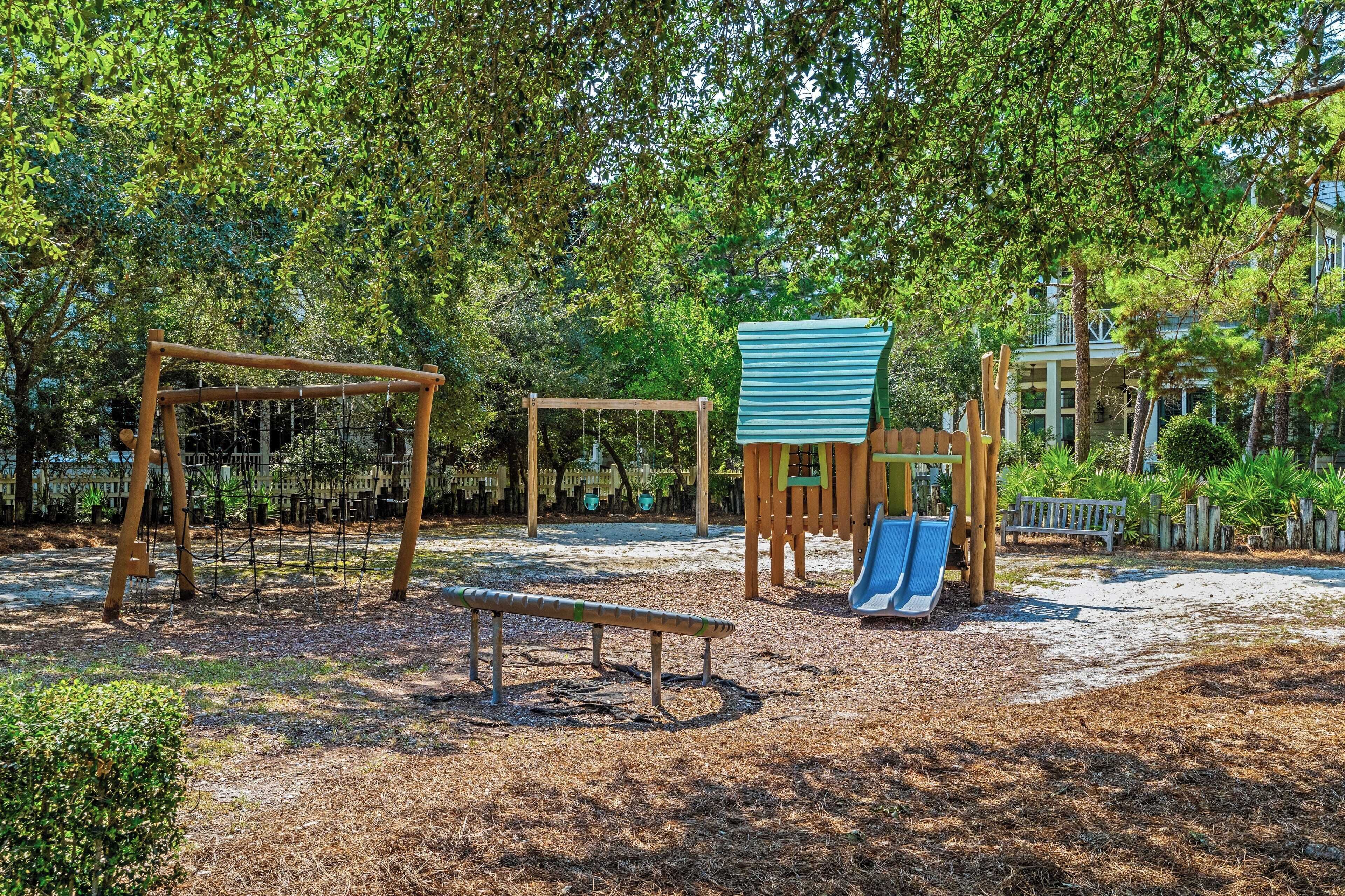 A playground with swings, a slide, and a climbing structure surrounded by trees.