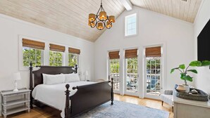 A bedroom with a large bed, wooden ceiling, and a view to the outside.