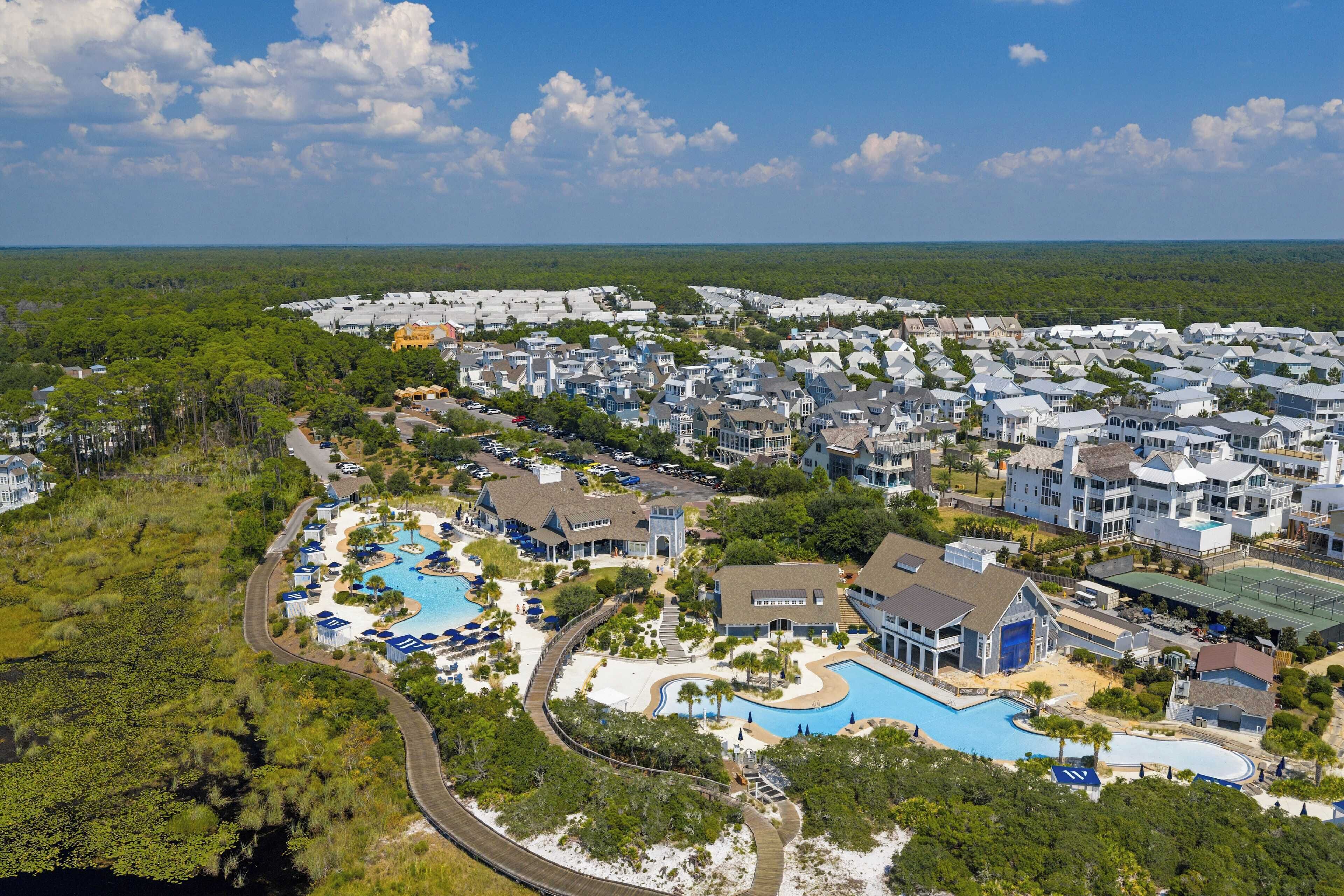 An aerial view of a resort with multiple buildings, a large swimming pool, and surrounding greenery.