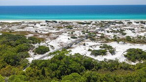 A coastal landscape with a wooden bridge connecting two areas, surrounded by dense greenery and a sandy beach.